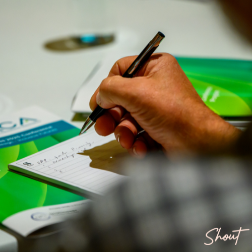 A person writing notes with a pen on paper at a desk.