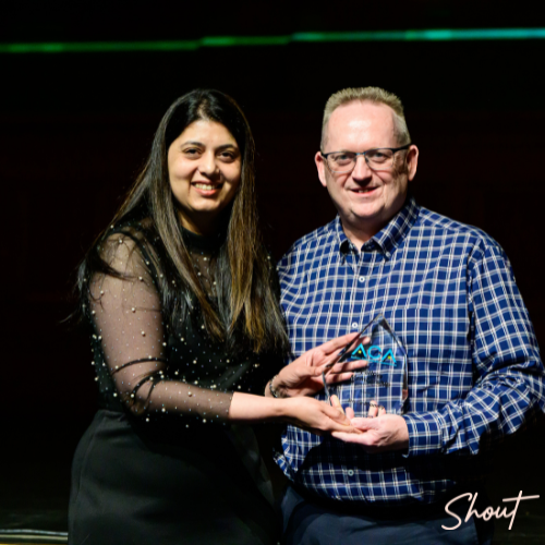 Two people smiling, holding a glass award together.