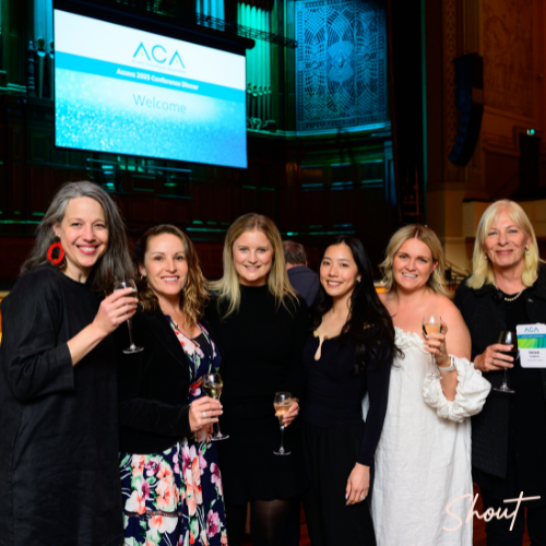 Group of six women smiling and holding drinks at an indoor event.