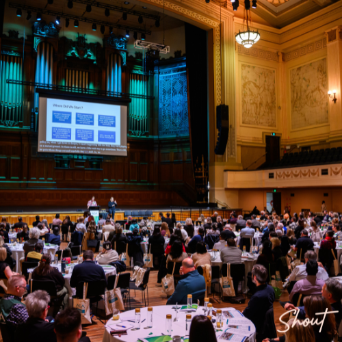 A large conference with attendees seated at round tables in a grand hall.