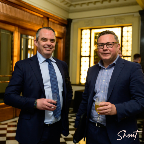 Two men in suits holding drinks at a formal event.