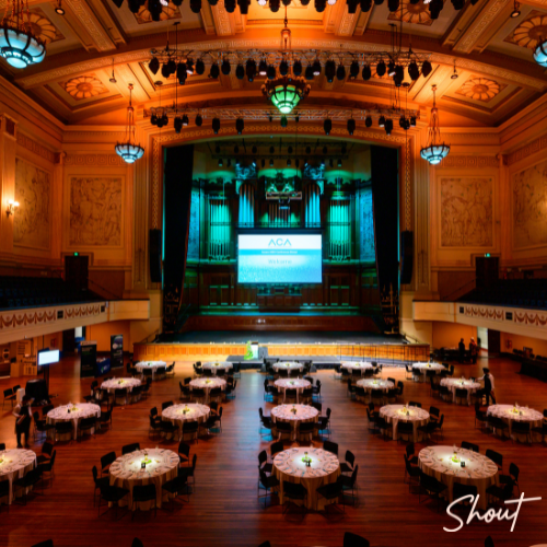 Empty banquet hall with round tables and stage lighting.