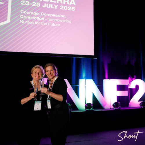 Two women smiling and posing at an event with large "NFE23" letters in the background.