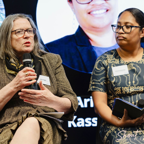 Two women speaking at a panel discussion, one holding a microphone.
