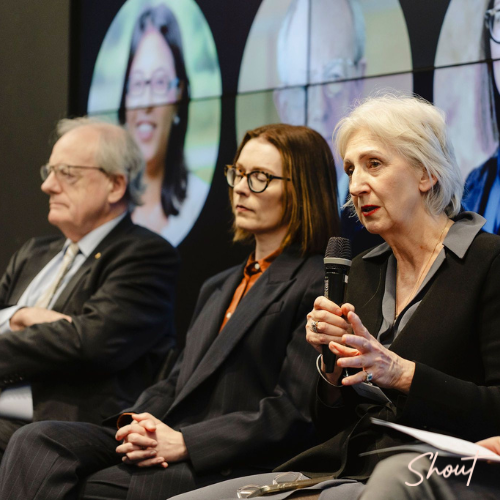 Three professionals engaged in a panel discussion, one speaking into a microphone.