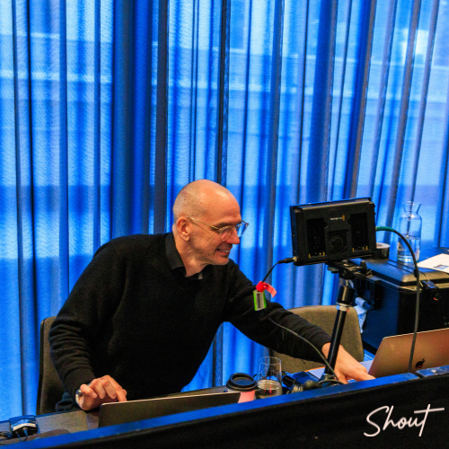 A man adjusting audio equipment in a studio with blue curtains.