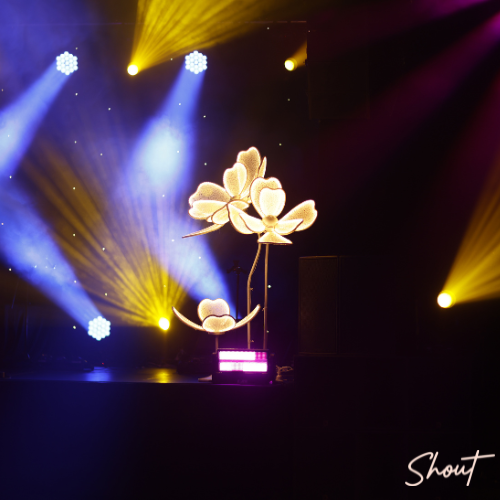 Illuminated flower sculpture on stage with vibrant lighting effects.