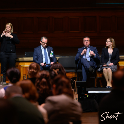 Panel discussion with four speakers addressing an audience in a formal setting.